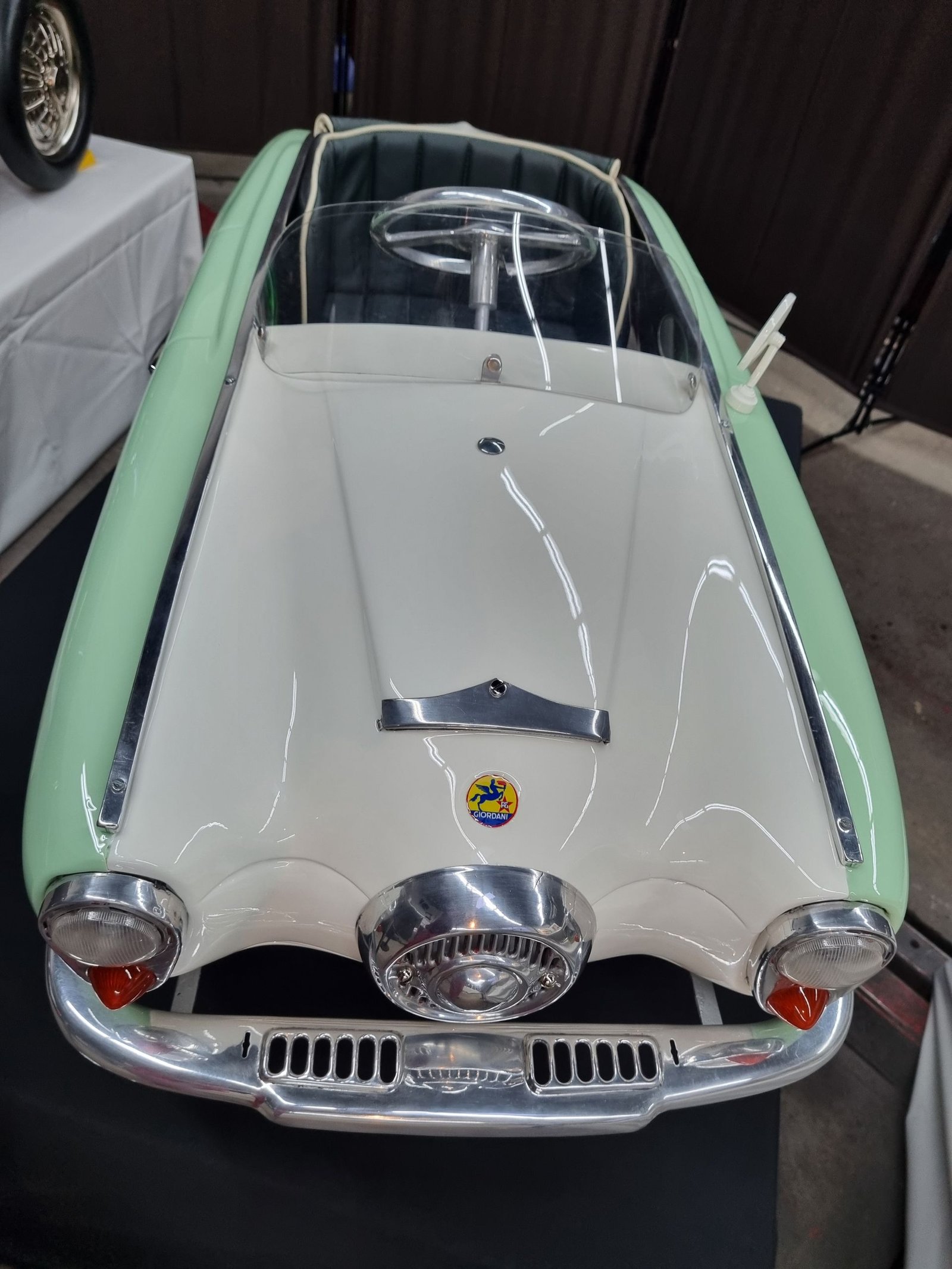 Auf einem Tisch steht ein grün-weißes Tretauto.